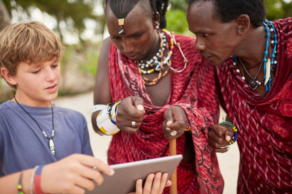 Boy teaching Maasai warriors to use a digital tablet.